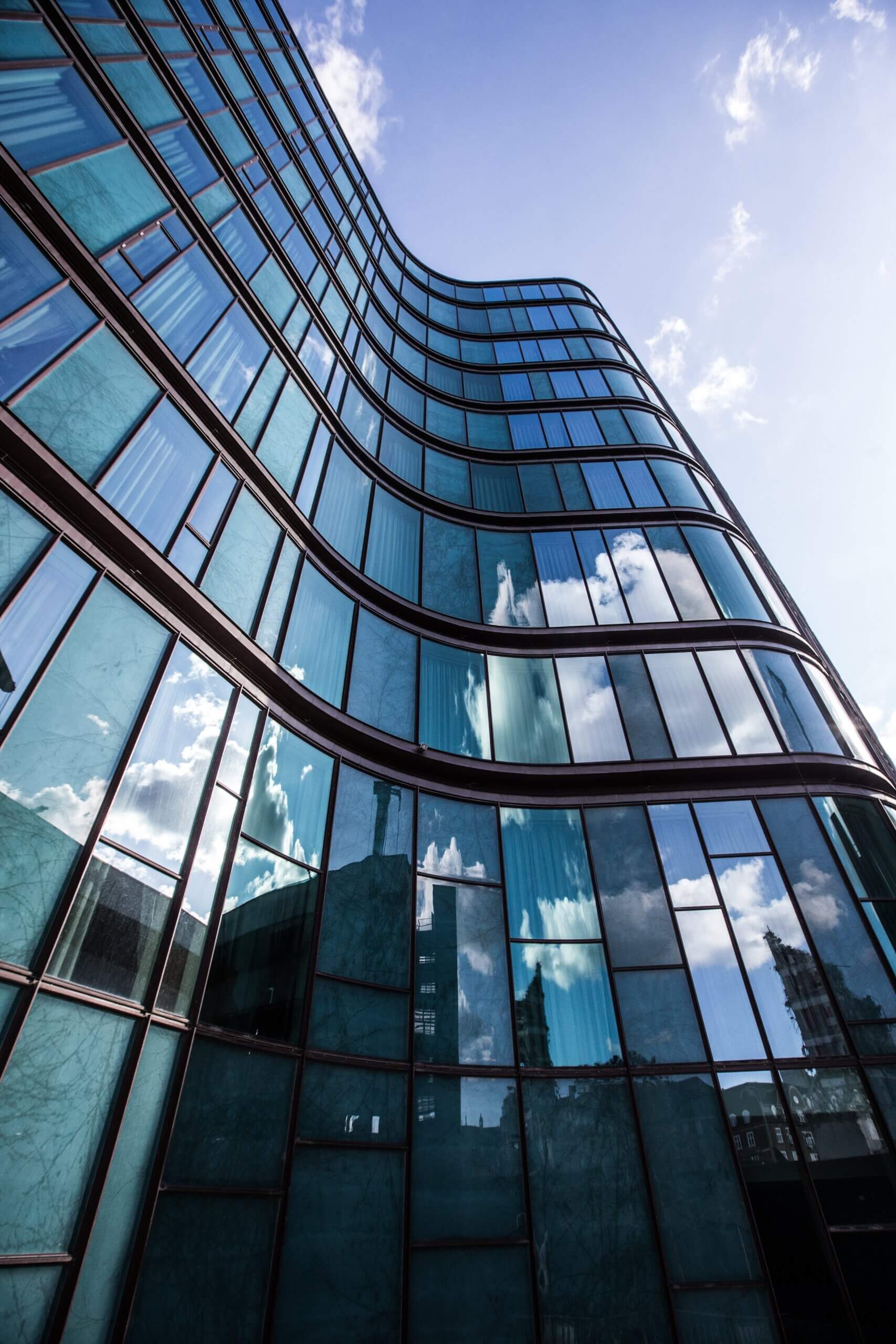 A vertical low angle shot of a high rise building in a glass facade with the reflection of the surrounding buildings